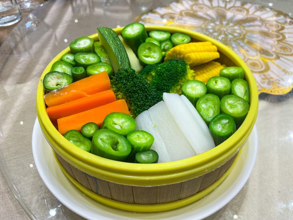 A vibrant selection of fresh vegetables in a bamboo bowl, ready for steaming and serving.